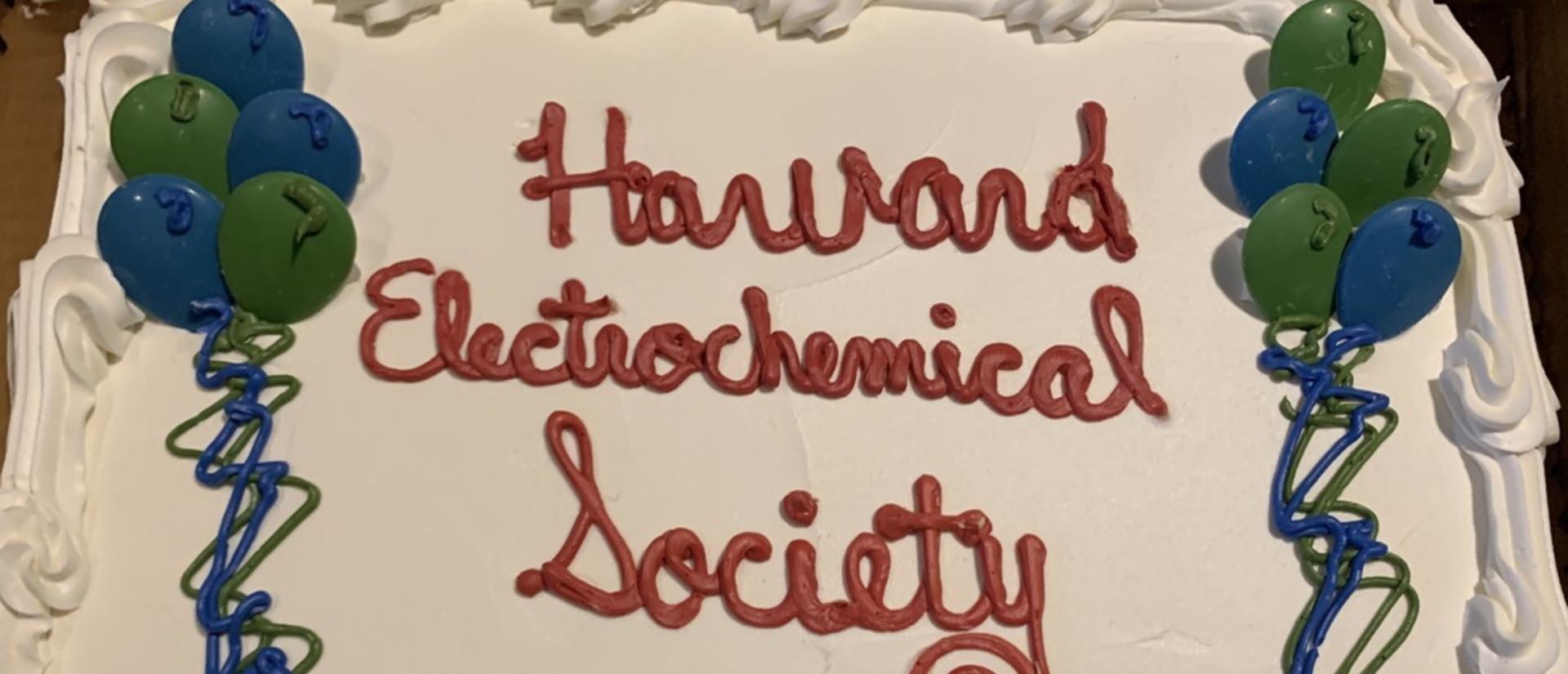 A white frosted cake with green and blue frosting balloons and red lettering saying Harvard Electrochemical Society